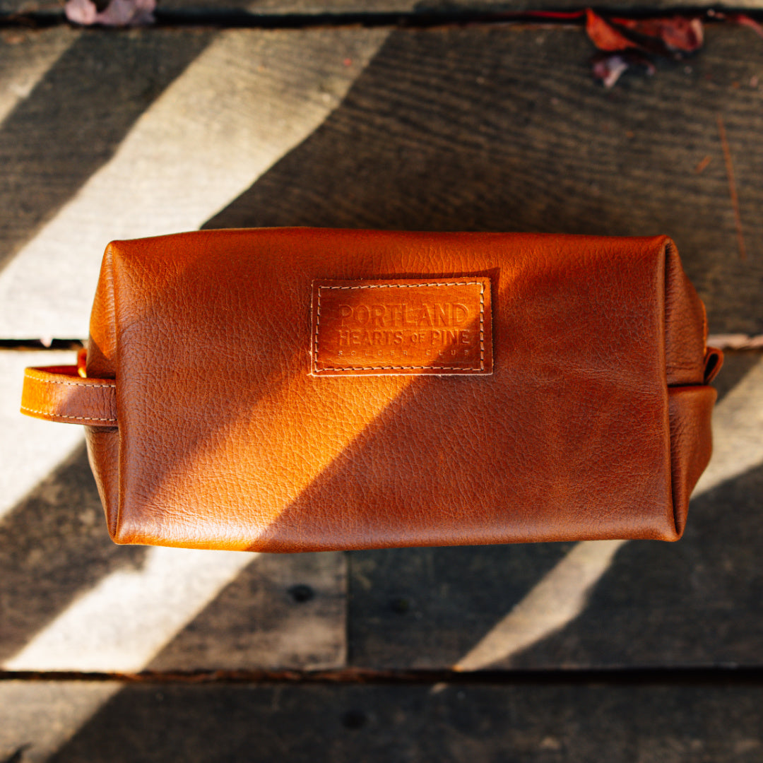 Brown leather pouch with a visible brand logo on a wooden surface