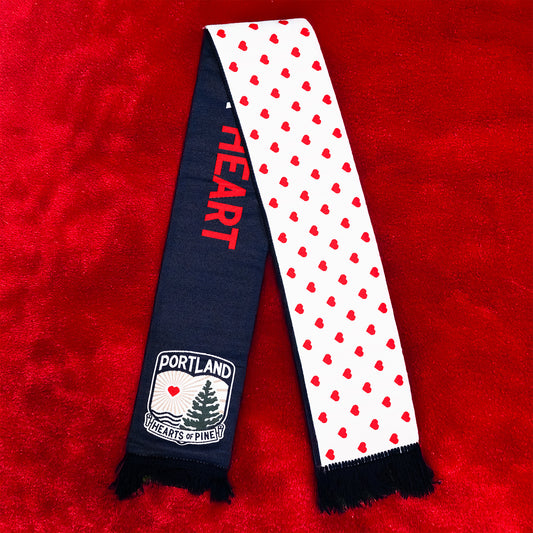 A scarf with a pattern of red hearts on a white background and the text 'HEART' on one end, with a logo that includes the word 'PORTLAND' on the other end.